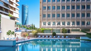 A swimming pool with lounge chairs and a view of modern buildings. - Hotel Madrid Chamartín Affiliated by Meliá (Madrid)