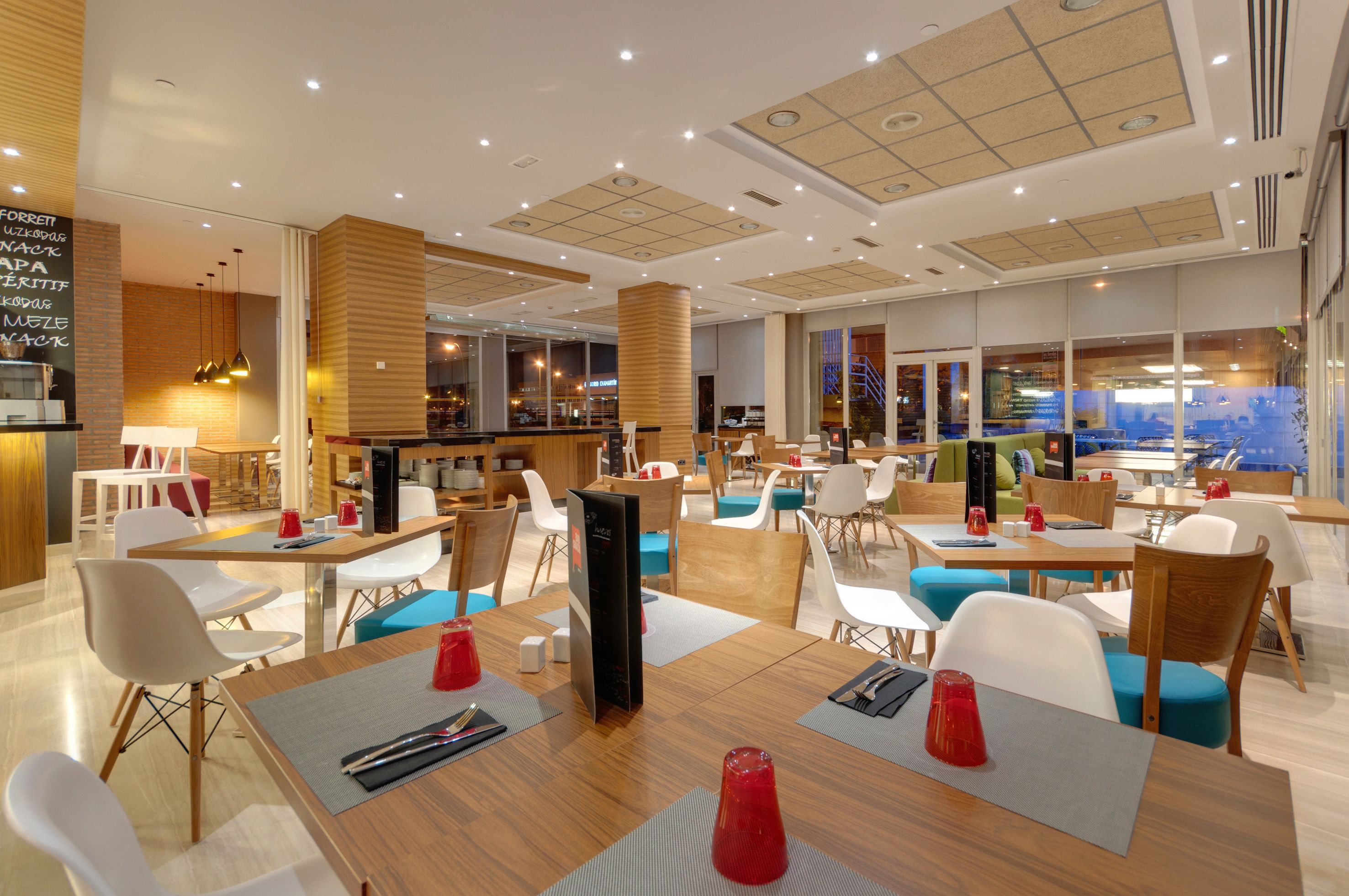 Ein modernes Restaurant mit Holztischen, weißen und blauen Stühlen und einer Bar.