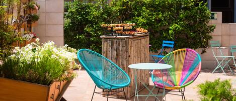 Zona de estar al aire libre con una mesa y sillas de madera, rodeada de vegetación y una exhibición de comida.