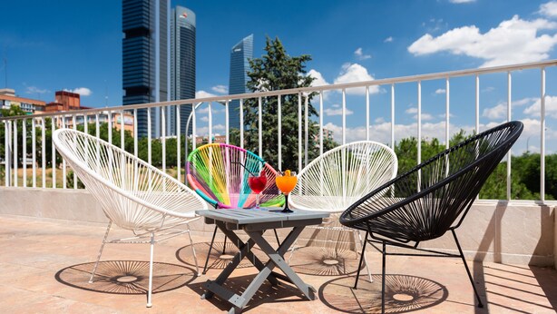 A terrace with two white wire chairs, a table, and a drink. - Hotel Madrid Chamartín Affiliated by Meliá (Madrid)