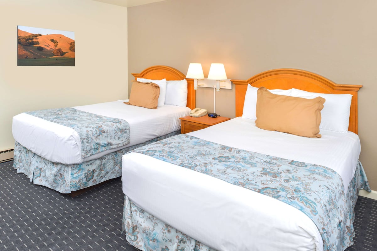 A hotel room with two single beds, a nightstand with a lamp, and a painting on the wall.