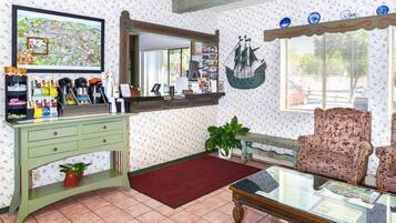 Une pièce avec une console verte, un tapis rouge, une table avec un plateau en verre, un fauteuil à motifs, une décoration maritime et une grande carte encadrée accrochée au mur.