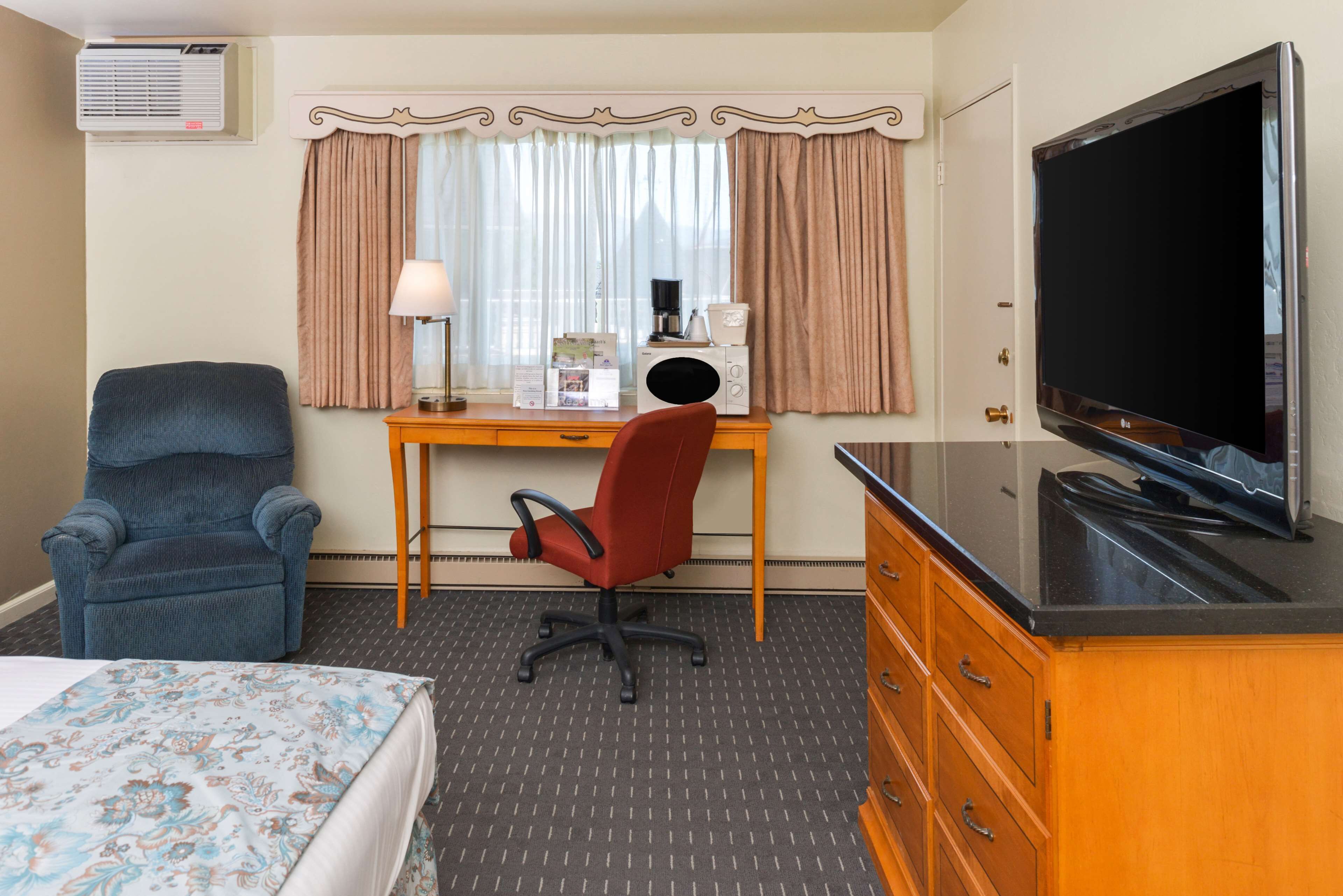 A hotel room with a bed, a desk with a computer, a TV, a chair, and a dresser.