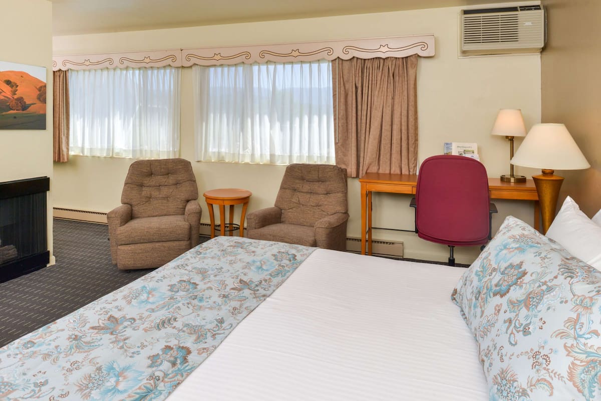 A hotel room with a bed, two armchairs, a small table, a desk with a lamp, and a painting on the wall.