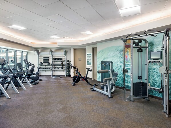 A gym with exercise equipment, a wall-mounted TV, and a large window.