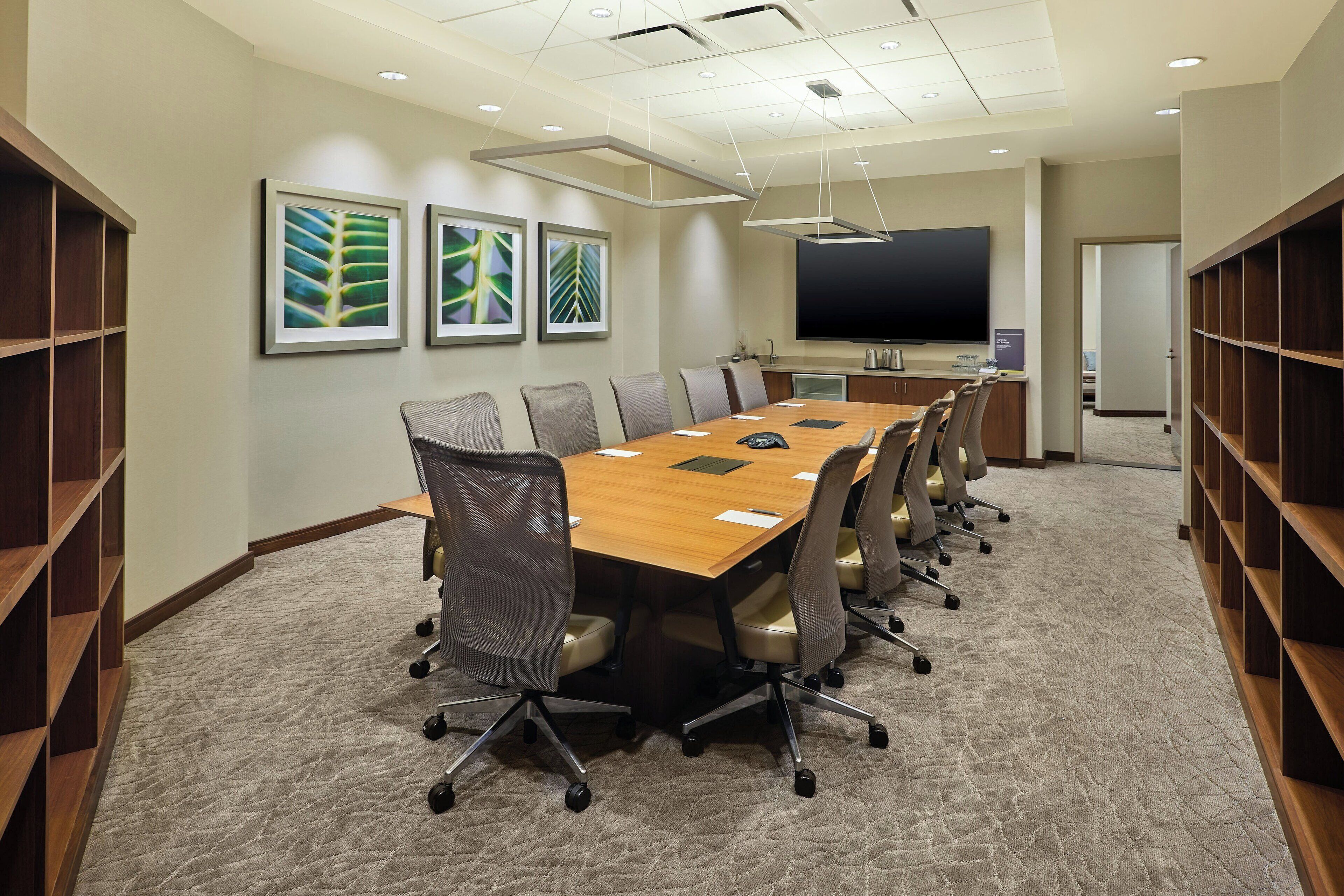 A conference room with a long table, chairs, a projector screen, and framed artwork on the walls.