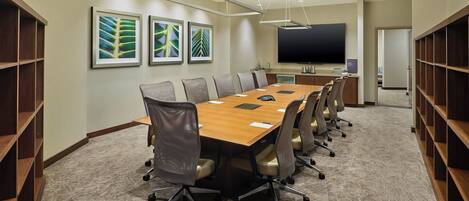 A conference room with a long table, chairs, a projector screen, and framed artwork on the walls.
