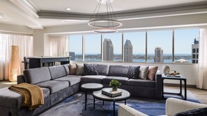 Un salon moderne avec un canapé d’angle, une table basse et une vue sur les gratte-ciel de la ville, visible à travers de grandes fenêtres.