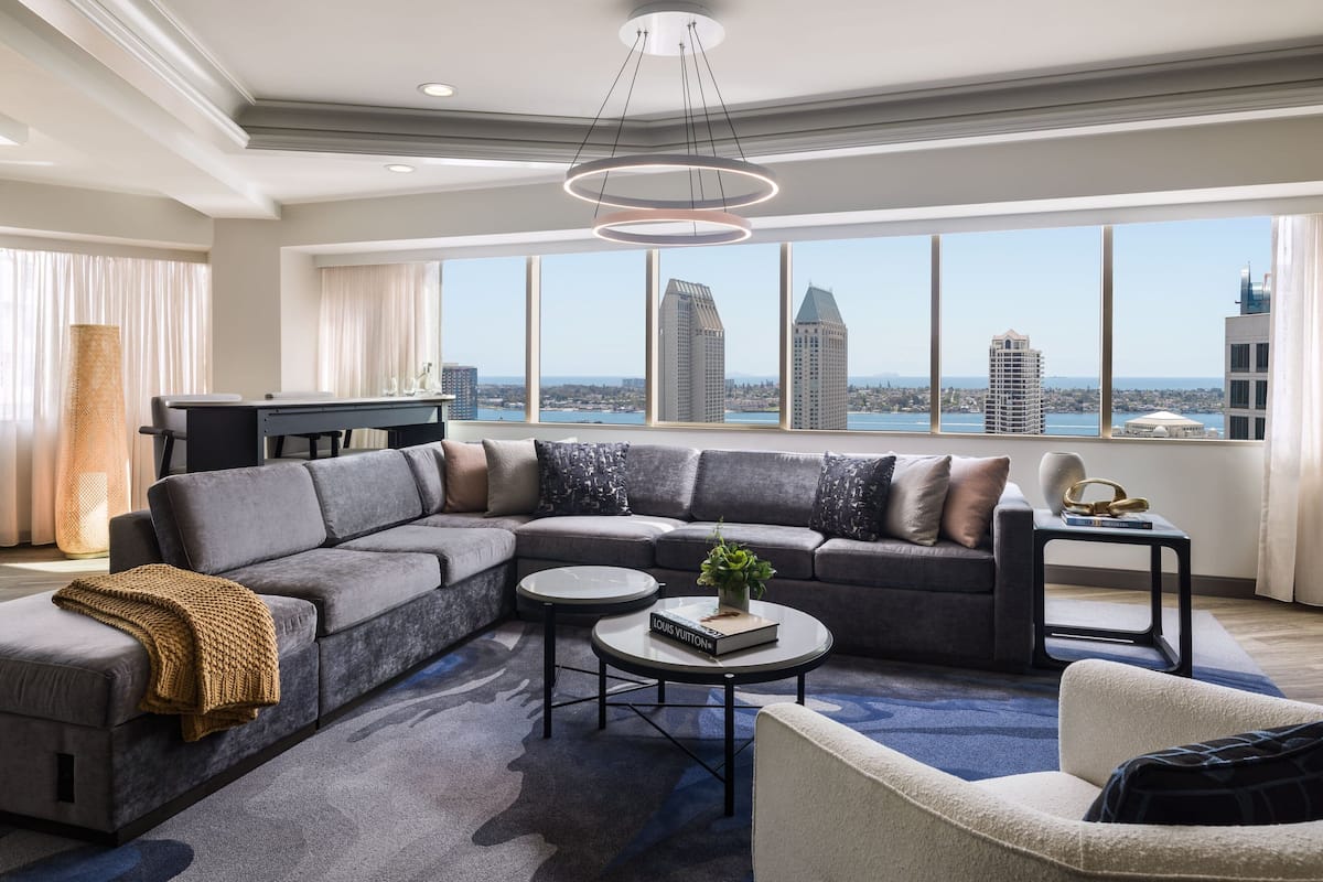 Ein modernes Wohnzimmer mit einer Eckcouch, einem Couchtisch und Blick auf die Skyline der Stadt durch große Fenster.