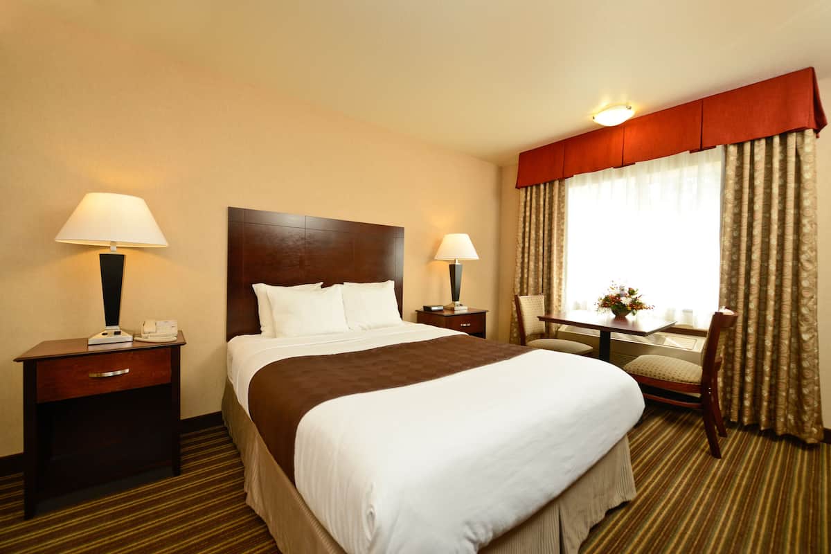 A hotel room with a large bed, two bedside tables with lamps, a chair, and a window with curtains.