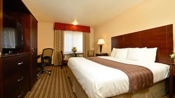 A hotel room with a large bed, a desk with a chair, a television, and a lamp.