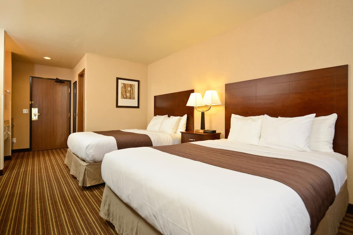 A hotel room with two beds, a wooden headboard, a nightstand with a lamp, and a striped carpet.