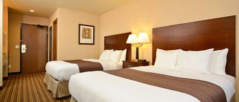 A hotel room with two beds, a wooden headboard, a nightstand with a lamp, and a striped carpet.