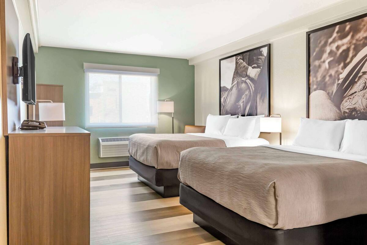 A hotel room with two beds, a desk, a TV, and artwork on the walls.