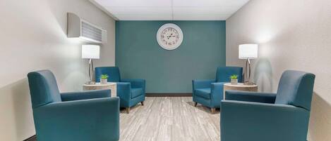 Una habitación con sillones azul turquesa, un reloj en la pared y una mesita con una lámpara y una planta.