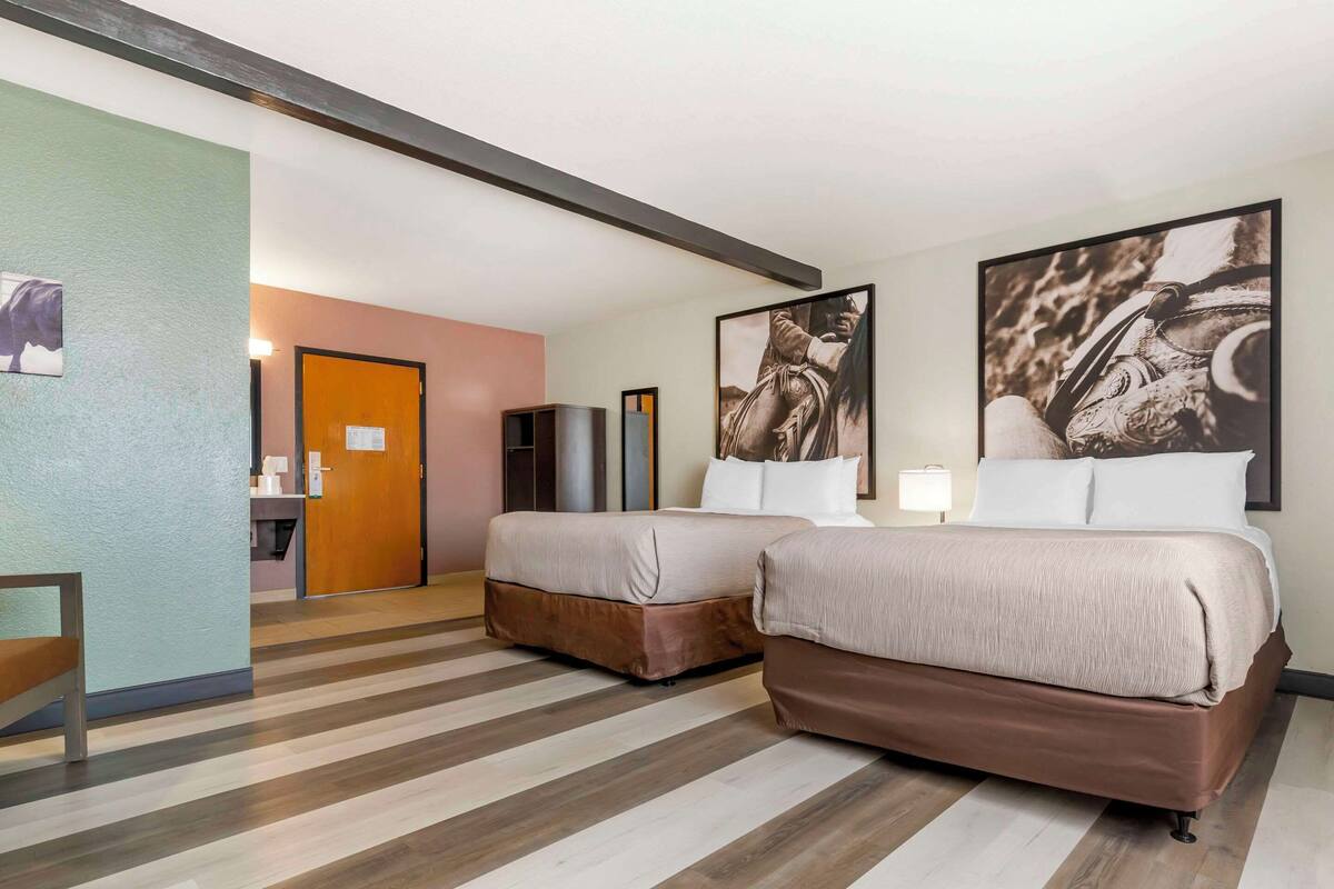 A hotel room with two beds, a wooden floor, a door, and a small table.