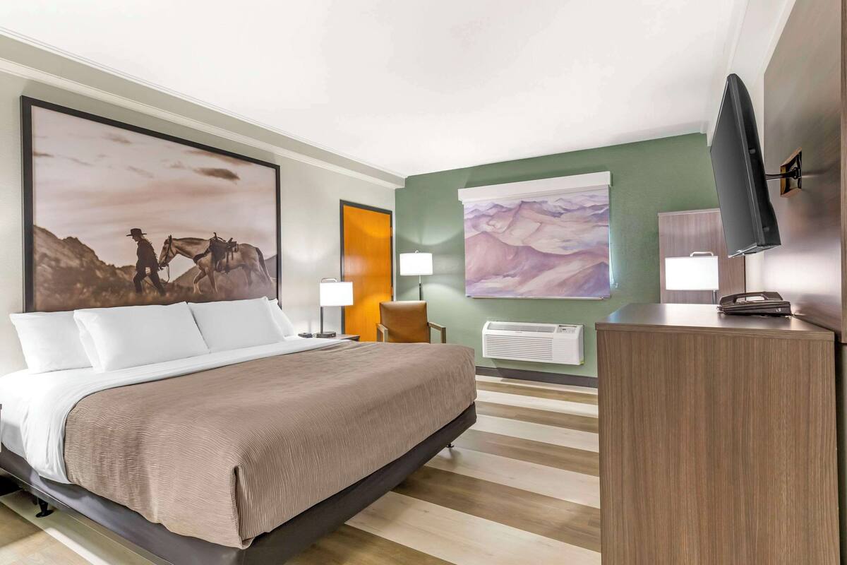 A hotel room with a large bed, a desk, a television, and two wall-mounted lamps.