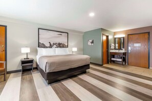 A hotel room with a large bed, bedside tables with lamps, a bathroom with a mirror, and a wooden floor.