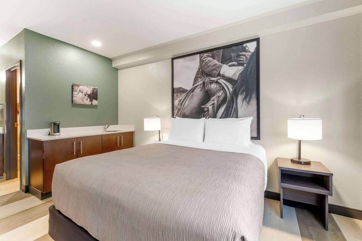 A hotel room with a large bed, a wooden dresser, a desk, and two bedside lamps.