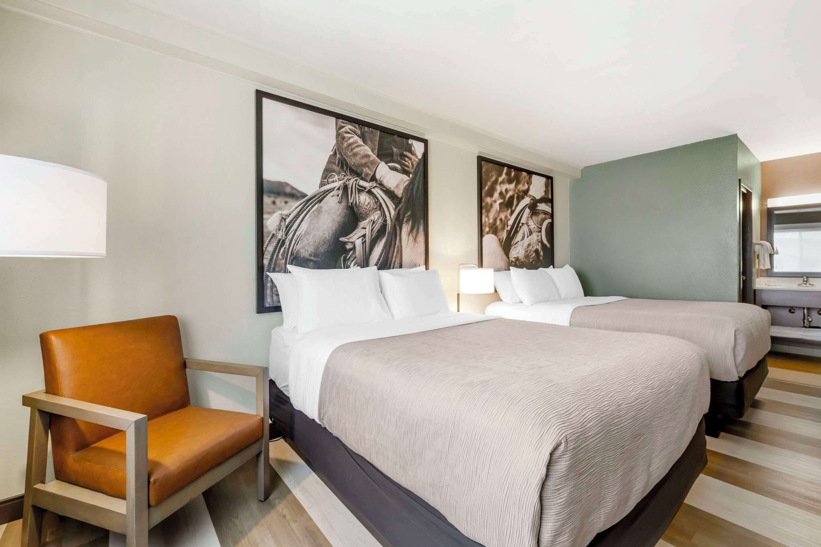 Une chambre d’hôtel avec deux lits, une chaise et des œuvres d’art accrochées aux murs.