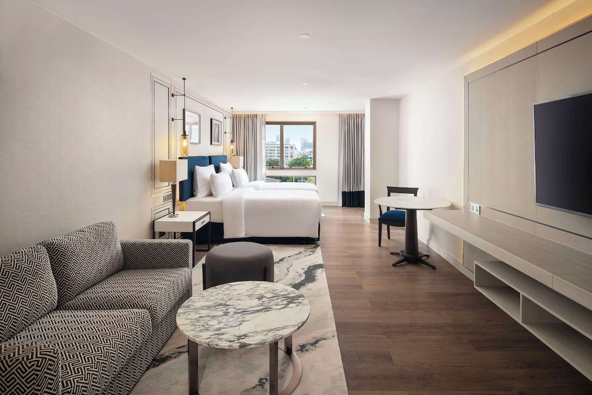 Habitación de hotel con cama, sofá, una mesita, televisor y vista a la ciudad.