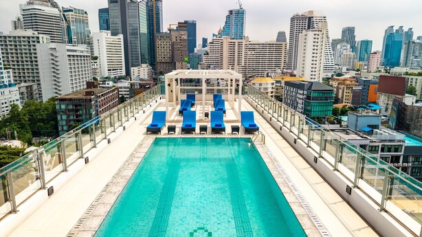 Piscina no terraço com cadeiras de descanso azuis e um horizonte urbano ao fundo.