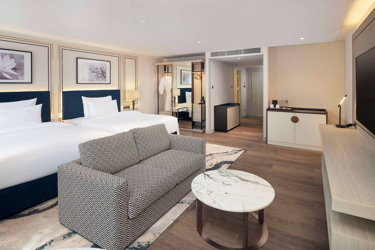 Una habitación de hotel con una cama grande, un sofá, una mesita, un escritorio y un televisor.