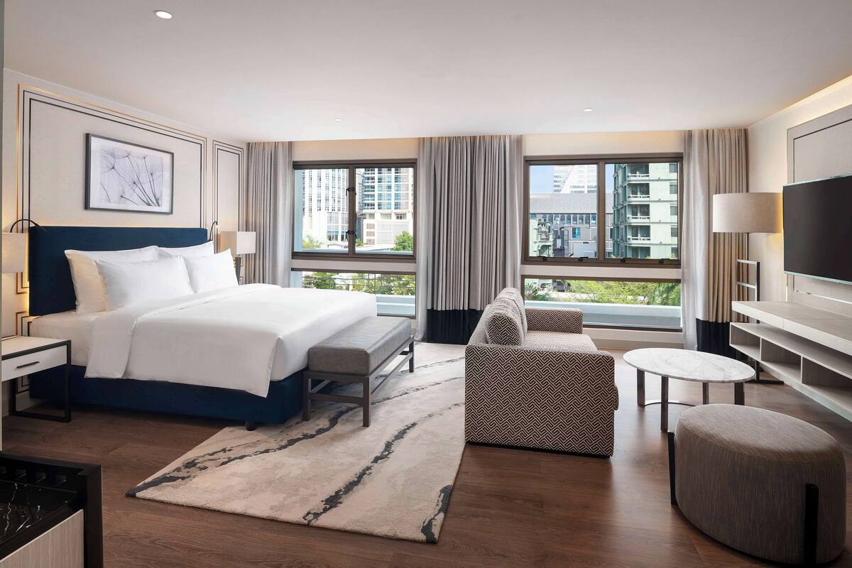 Una habitación de hotel moderna con una cama grande, un sofá, una mesita y un televisor.
