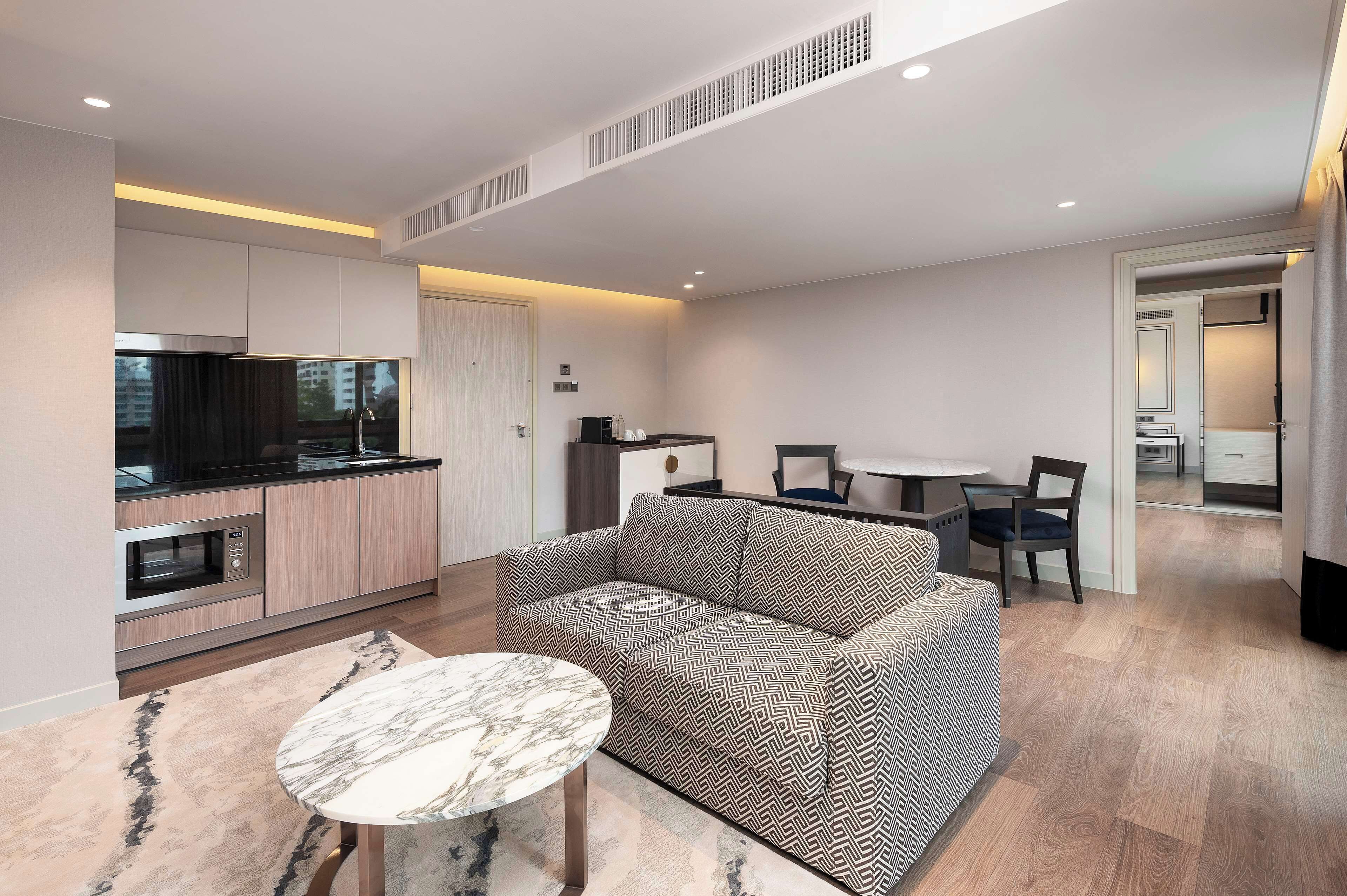 A modern living room with a sofa, a marble table, and a kitchen area with cabinets and appliances.