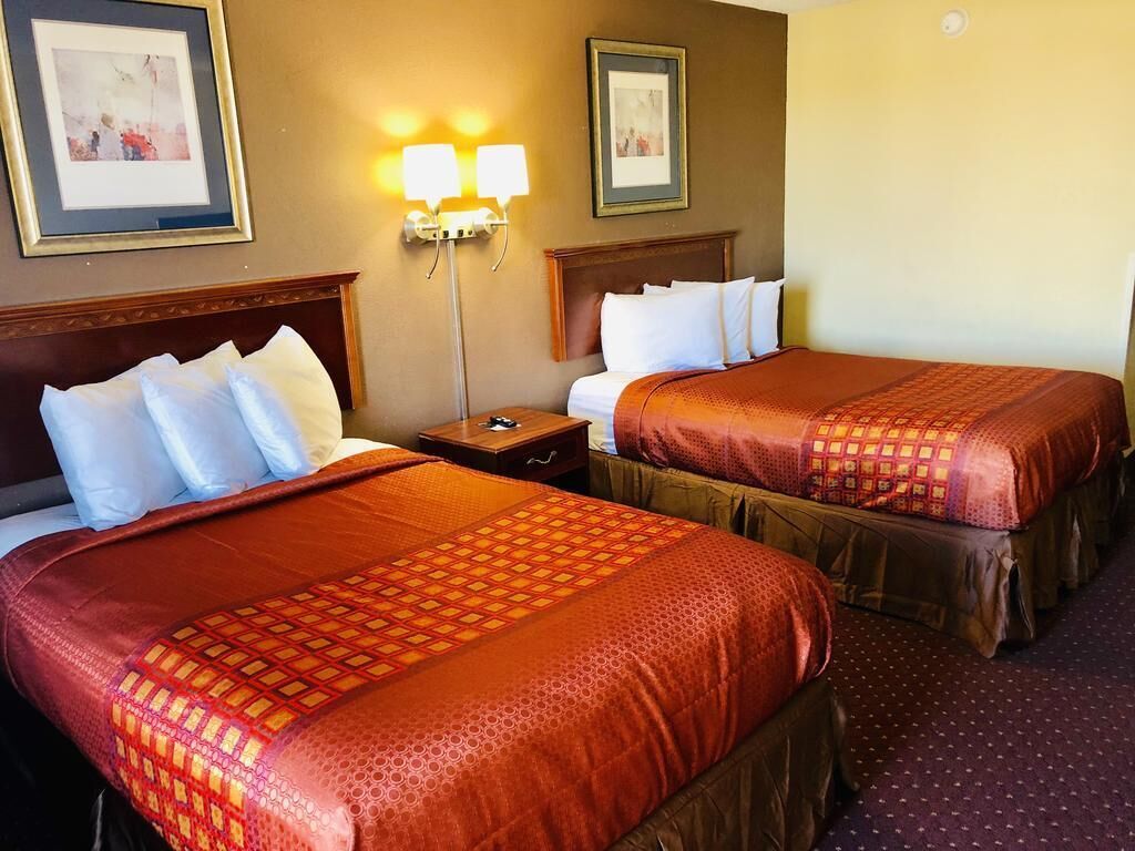 Two double beds with matching headboards, a nightstand, wall-mounted lamps, and framed pictures on the wall.