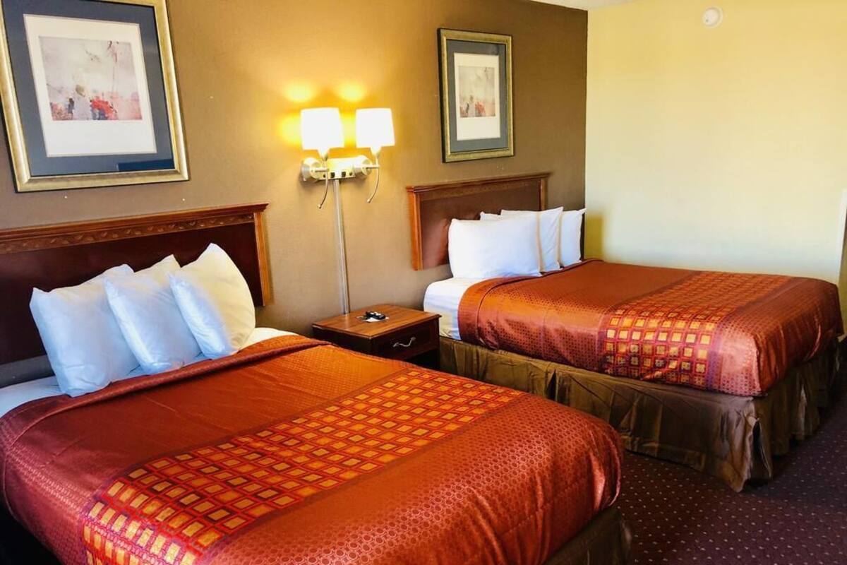 Two double beds with matching headboards, a nightstand, wall-mounted lamps, and framed pictures on the wall.