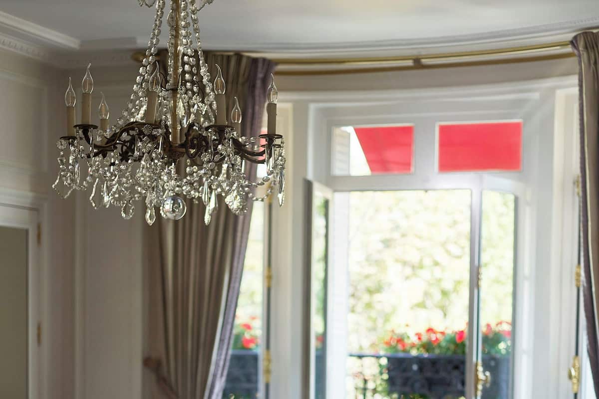Een slaapkamer met een groot bed, een kroonluchter, een stoel en uitzicht op een balkon met bloemen.