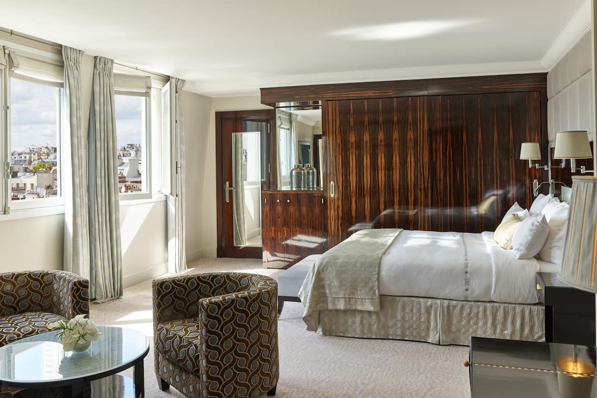 Hotelkamer met een bed, zithoek met een tafel en stoelen, een kledingkast en uitzicht op de stad vanuit het raam.
