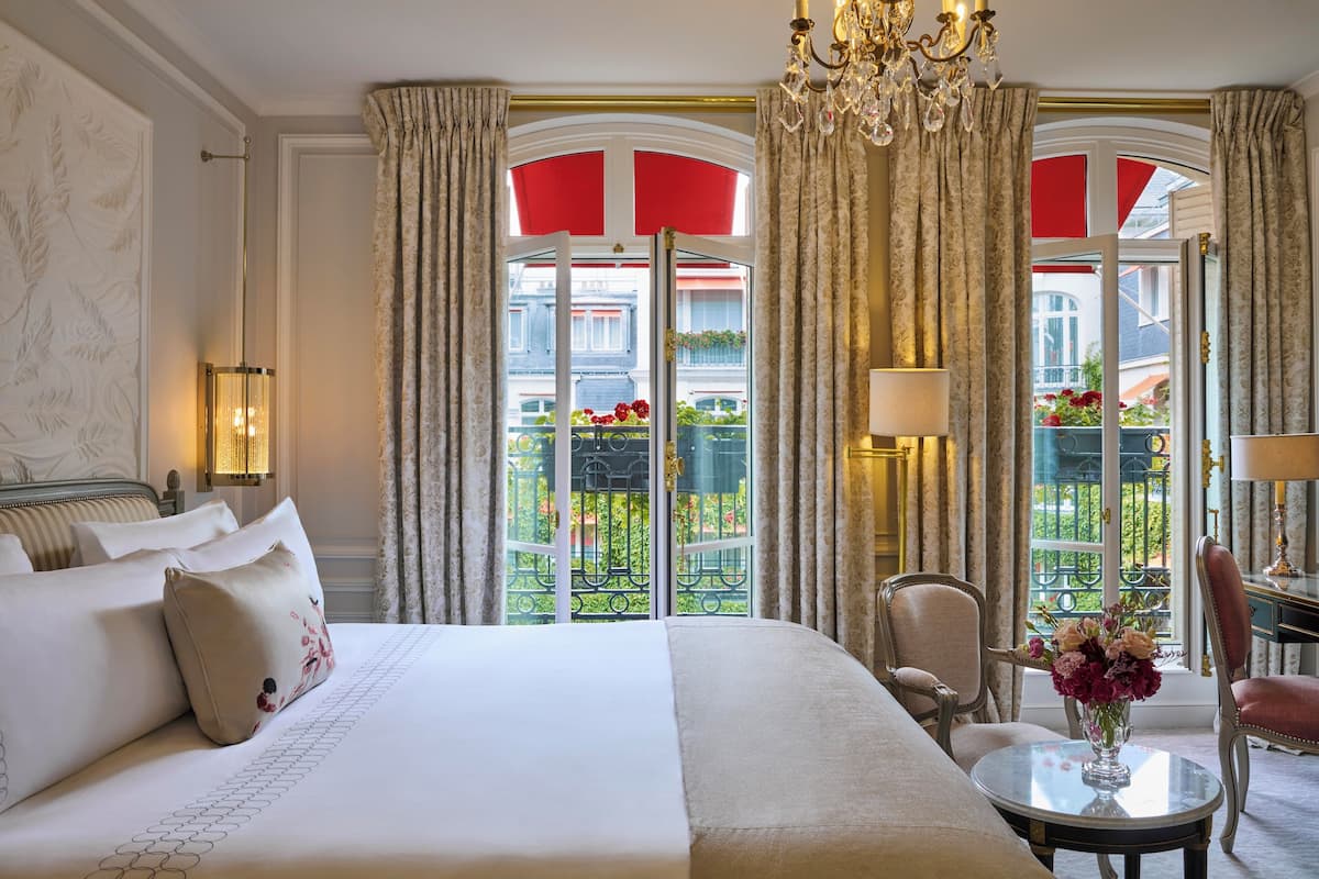 Hotelkamer met een groot bed, een zithoek met een tafel en uitzicht op een balkon met rode luifels.