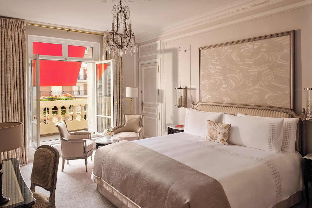 Een ruime slaapkamer met een groot bed, een kroonluchter, uitzicht op een balkon en een klassiek design.