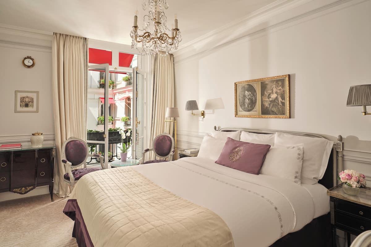 Een stijlvol ingerichte slaapkamer met een groot bed, een kroonluchter, een bureau met lamp en uitzicht op het buitenbalkon.