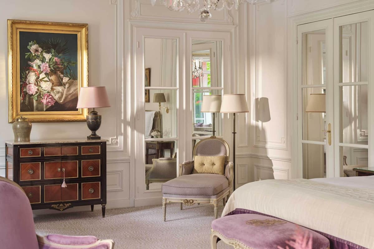 A room with a bed, a chair, a dresser, a chandelier, and a mirror.