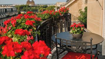 A terrace with red flowers, a table, and a chair. In the background, the Eiffel Tower is visible.