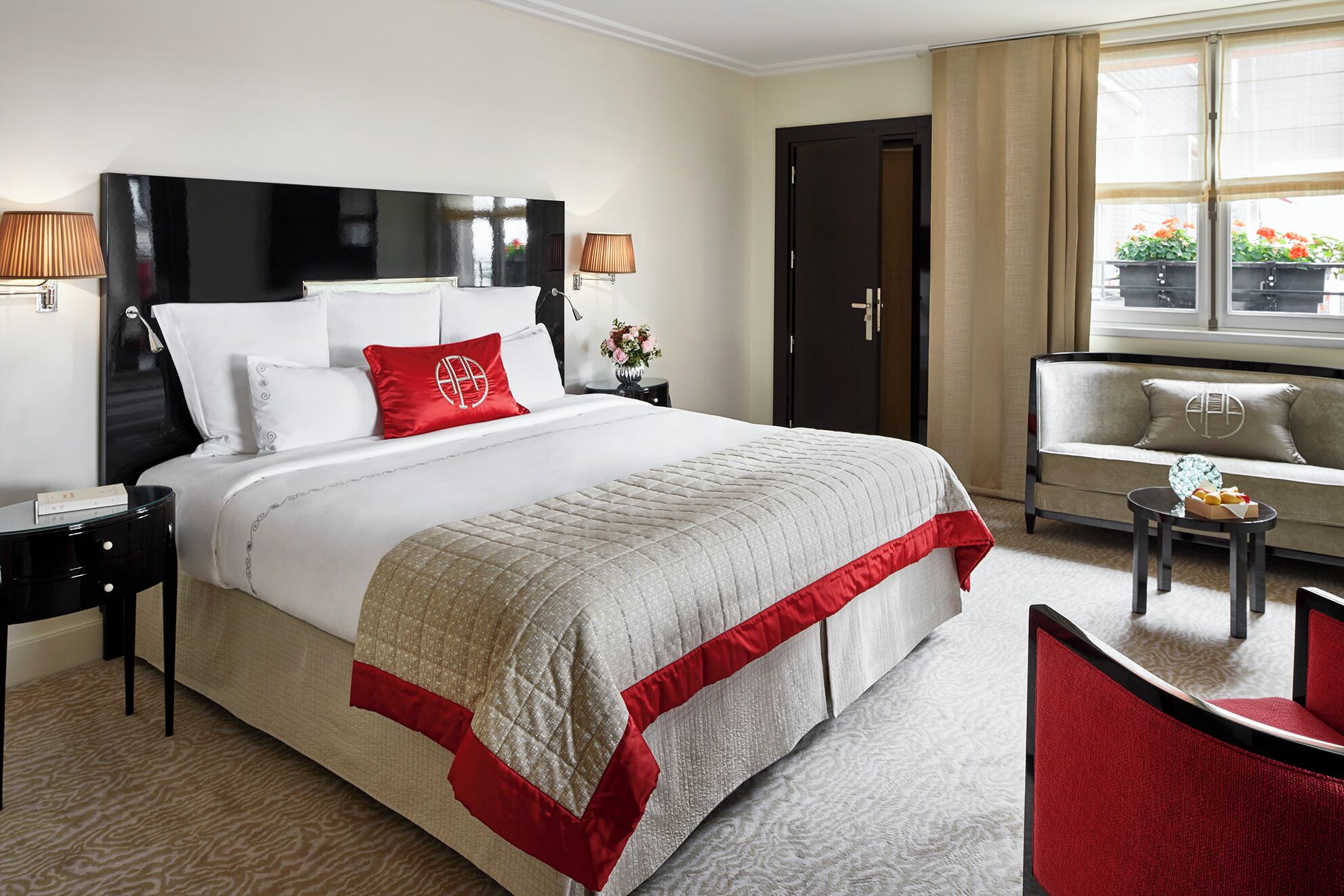 Une chambre d’hôtel avec un grand lit, deux tables de chevet, une petite table, un canapé, une chaise et une fenêtre avec des rideaux.