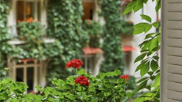 A balcony with a view of a building covered in ivy, potted plants, and red flowers.