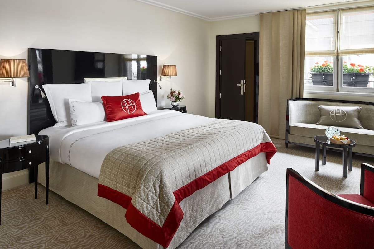Een hotelkamer met een groot bed, een bank, een tafeltje met een vaas en een raam met gordijnen.