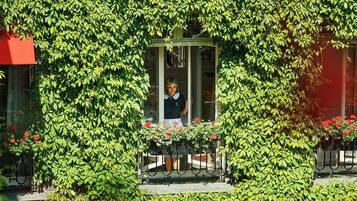 A building with a green ivy-covered facade, a balcony with a red awning, and a person standing on the balcony.