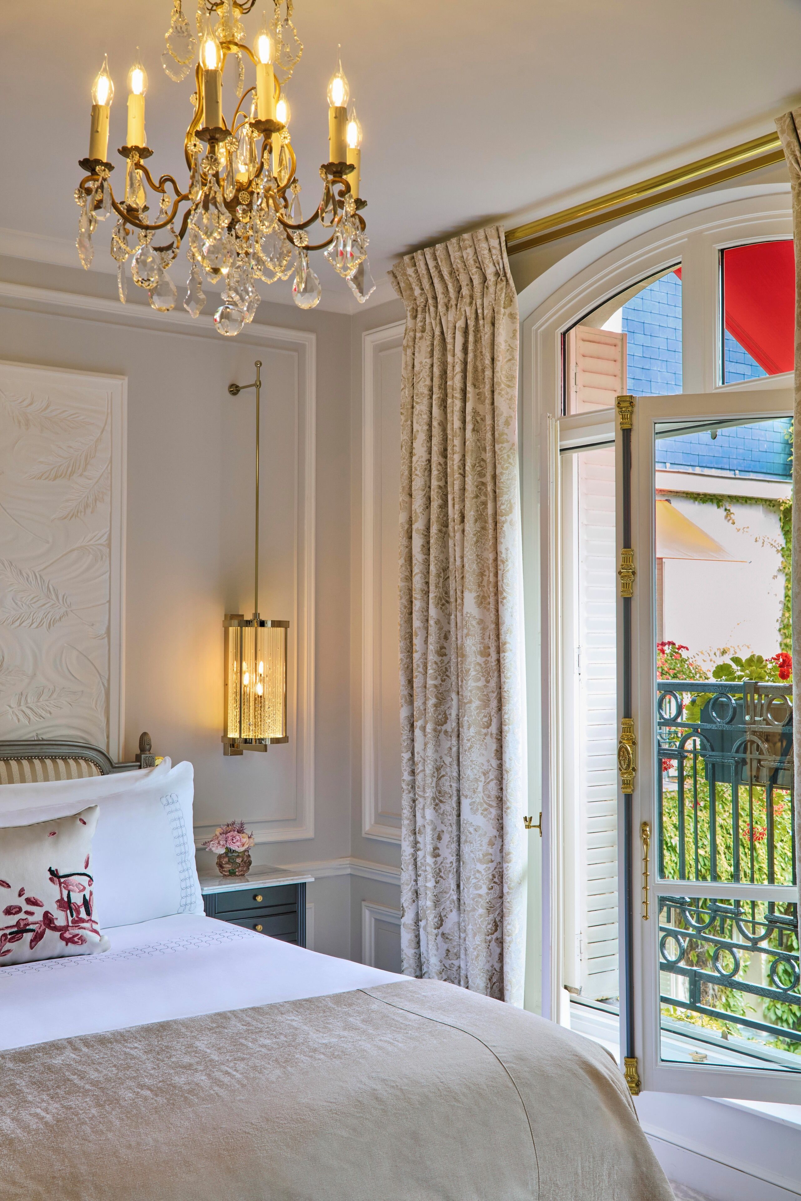 Une chambre à coucher avec un grand lit, un lustre, une table de chevet avec une lampe et une fenêtre avec des rideaux.