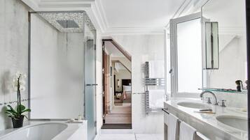 A modern bathroom with a large bathtub, two sinks, and a walk-in shower.