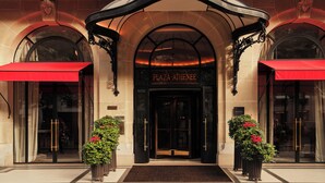 The entrance of Plaza Athenee with a red awning, arched windows, and potted plants. - Hôtel Plaza Athénée - Dorchester Collection (Paris)
