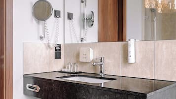 A modern bathroom with a marble sink, a mirror, a towel rack, and a shower area.