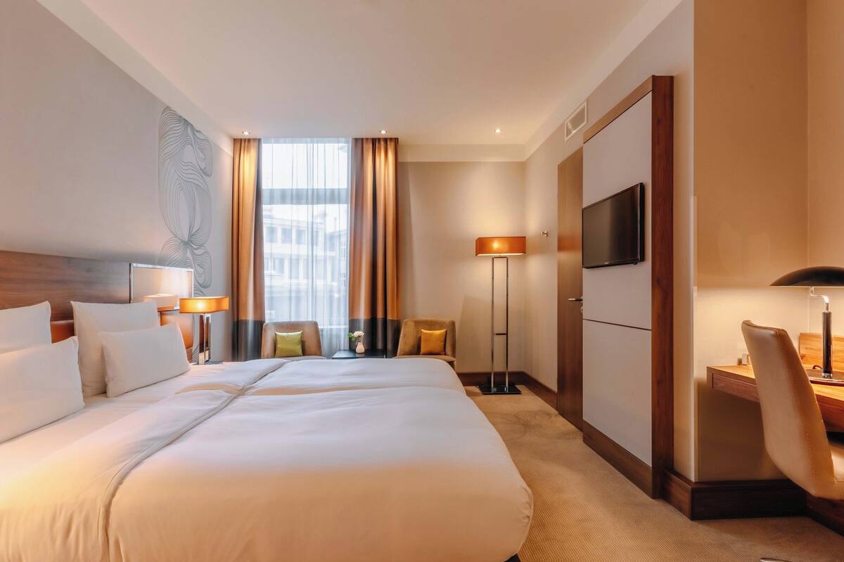 Une chambre d’hôtel avec un grand lit, un bureau, une chaise, une télévision et une fenêtre avec des rideaux.