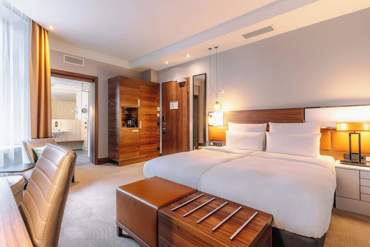 Une chambre d’hôtel avec un grand lit, une armoire en bois, un bureau avec une chaise et une table de chevet avec une lampe.