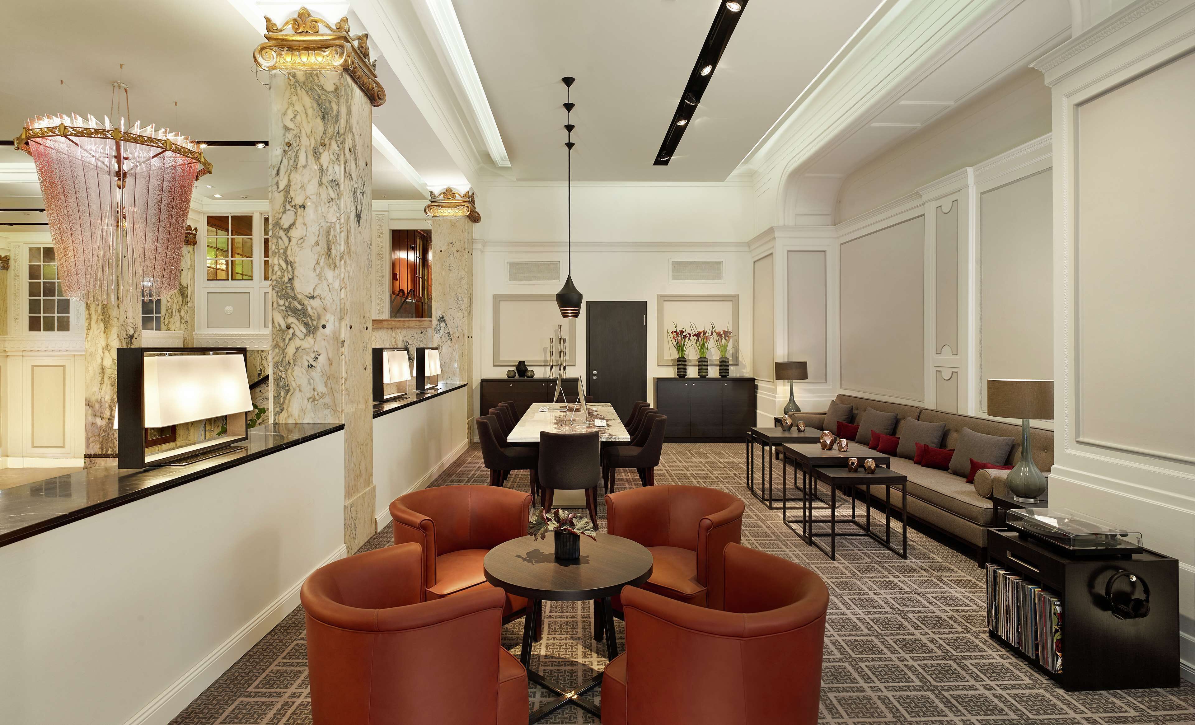 Un lobby de hotel lujoso con columnas de mármol, una gran araña, un mostrador de recepción, una zona de estar con sofás y una mesa de centro, y una alfombra estampada.