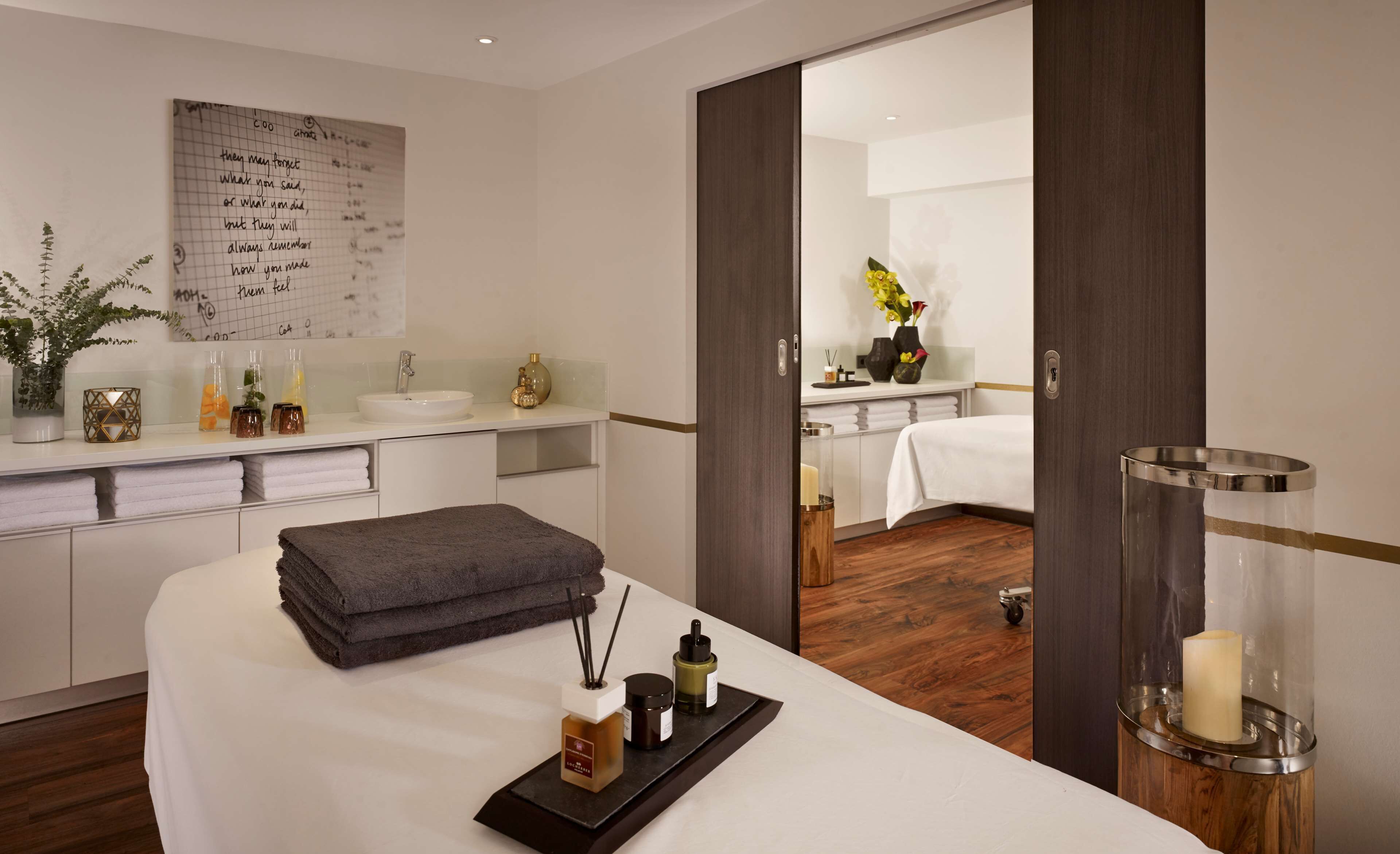 A modern hotel room with a large bed, a bedside table with toiletries, a mirror, and a view into the bathroom.